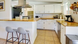 A modern kitchen with white cabinets, a wooden countertop, and two bar stools. - Joshua Tree Home w/ Patio - 5 Mi to National Park! (Joshua Tree)