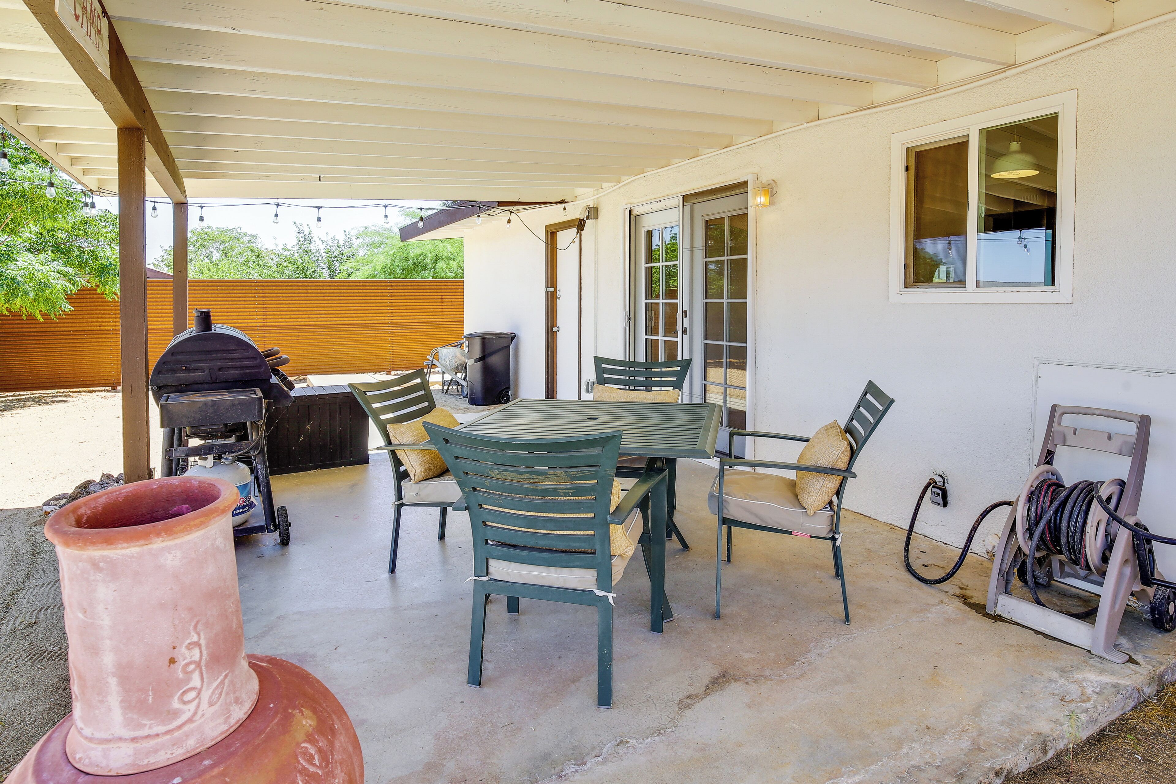 A covered patio with a table and chairs, a grill, and a hose reel.
