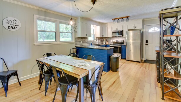 A modern kitchen with white cabinets, a blue island, stainless steel appliances, and a dining area with a wooden table and metal chairs. - Pet-friendly Greenville Vacation Rental w/ Deck! (Greenville)
