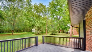 A wooden deck with a railing, a brick wall, and a view of a green lawn and trees. - Pet-friendly Greenville Vacation Rental w/ Deck! (Greenville)