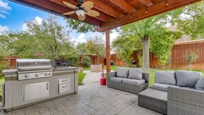 An outdoor patio with a built-in grill, wicker furniture, and a ceiling fan. - Upscale Pflugerville Paradise w/ Private Pool! (Pflugerville)