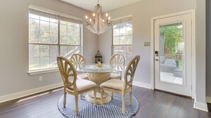 A dining area with a round glass table, four chairs, a chandelier, and large windows. - Upscale Pflugerville Paradise w/ Private Pool! (Pflugerville)