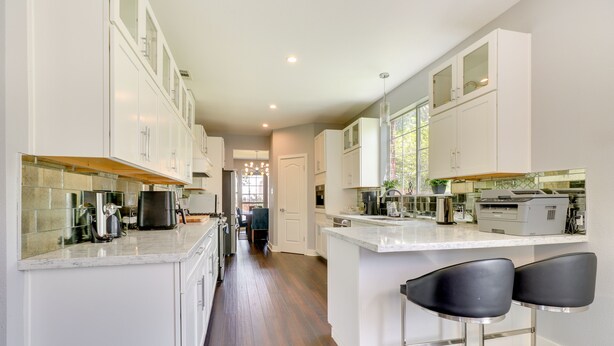 A modern kitchen with white cabinets, a central island with bar stools, and a view into the dining area. - Upscale Pflugerville Paradise w/ Private Pool! (Pflugerville)