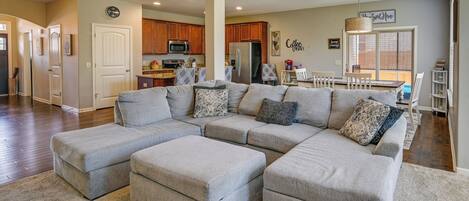 A spacious living room with a sectional sofa, a dining area, and a kitchen in the background.