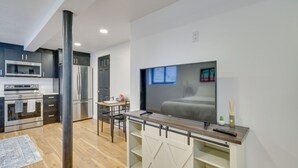 Een moderne keuken met roestvrijstalen apparatuur, een eethoek met tafel en stoelen, en een aan de muur bevestigde televisie.