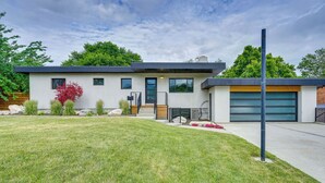 Een modern huis met twee verdiepingen, een garage, een verzorgd gazon en een bloeiende rode plant.
