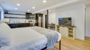 Een moderne slaapkamer met een groot bed, een televisie en een kitchenette op de achtergrond.