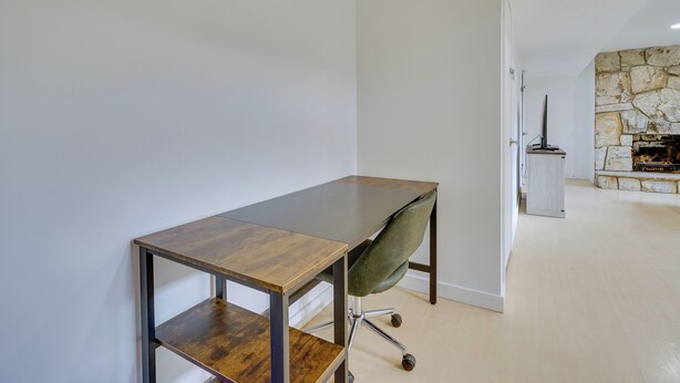 Una habitación moderna con un escritorio de madera, una silla verde y una chimenea de piedra.