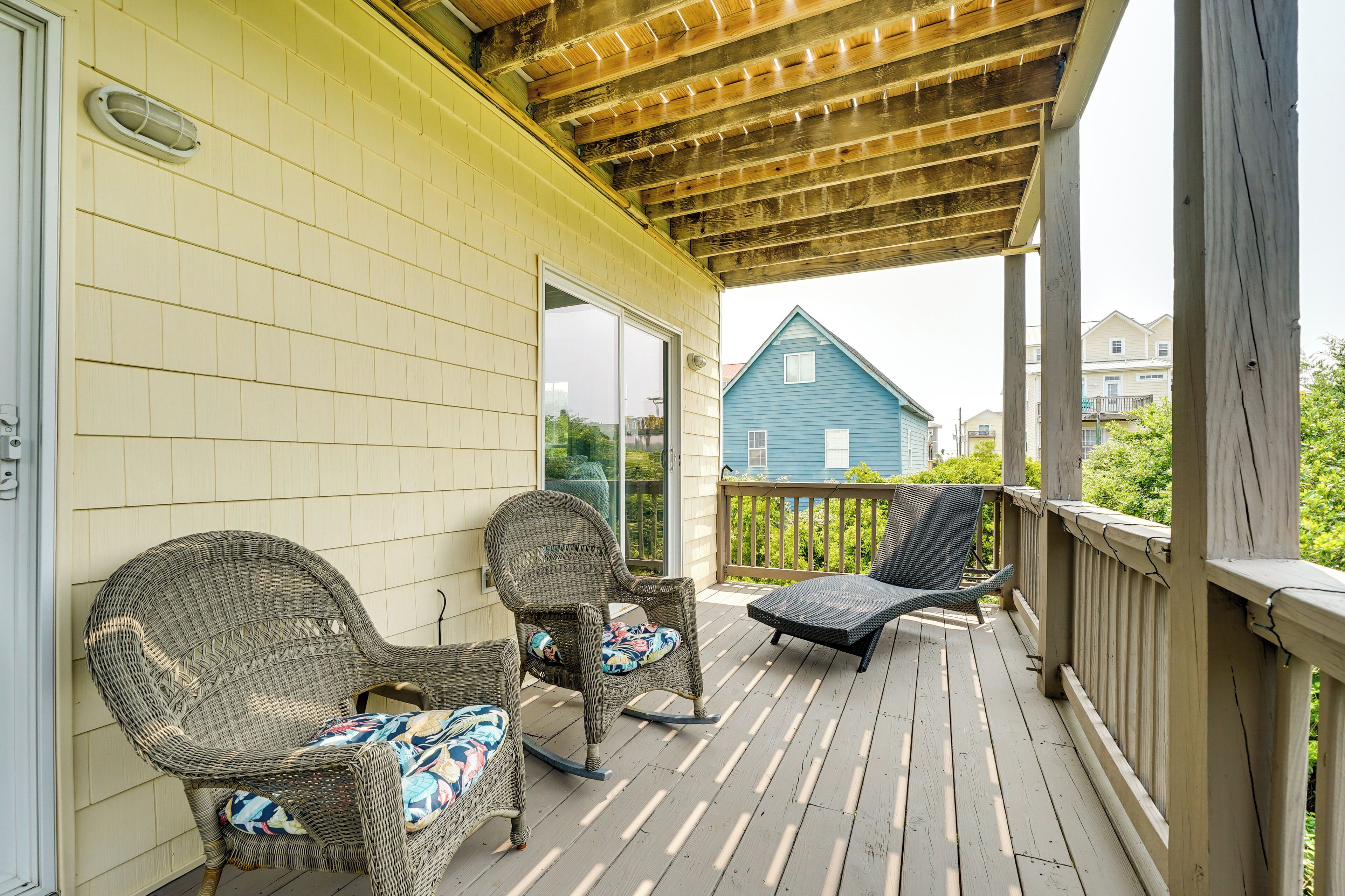A covered porch with wicker furniture and a view of a blue house in the background.