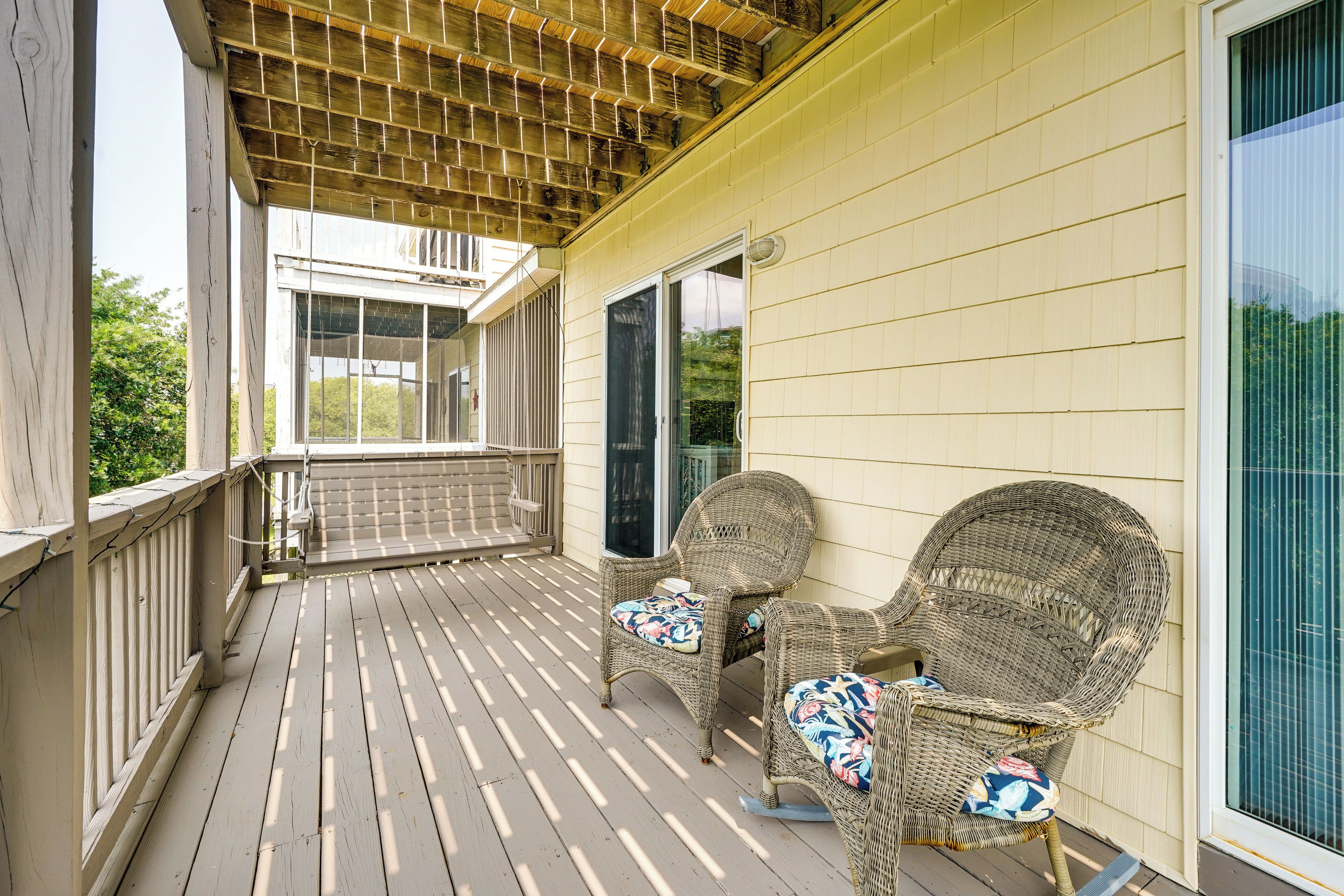 A covered porch with two wicker chairs and a wooden railing.