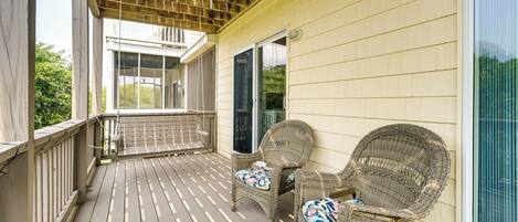 A covered porch with two wicker chairs and a wooden railing.