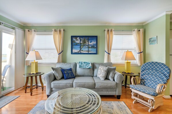 A living room with a sofa, armchair, two lamps, a painting, and a window with curtains. - Coastal Murrells Inlet Condo With Balcony! (Murrells Inlet)