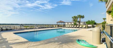 A rectangular pool with a sandy deck, surrounded by lounge chairs and palm trees.