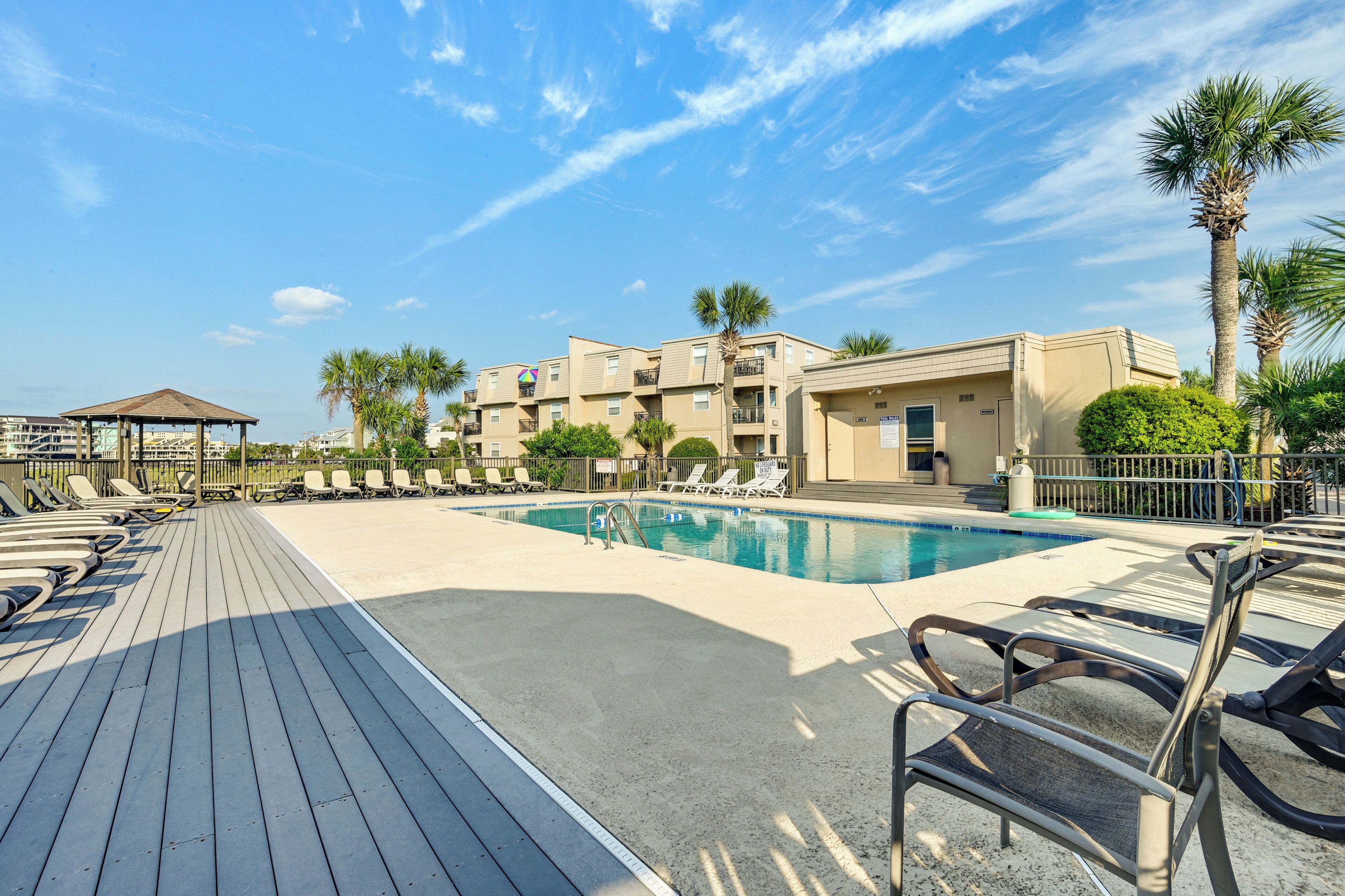 Un espace piscine comprenant des chaises longues, un belvédère et un bâtiment doté de balcons.