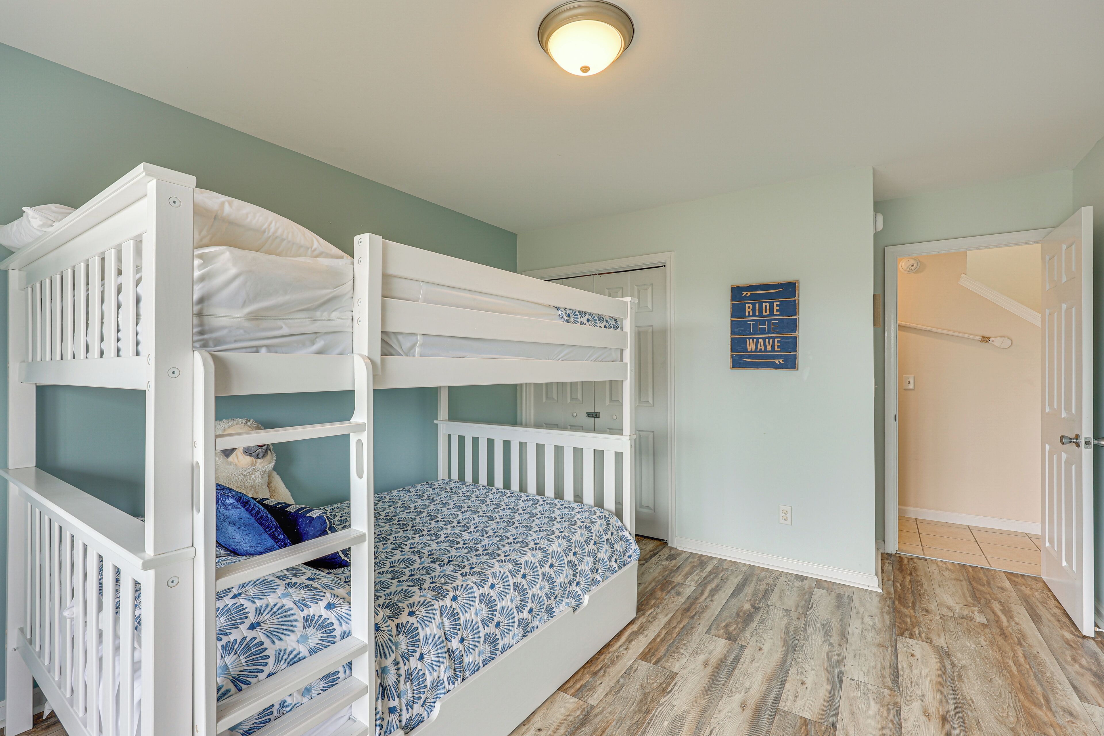 Ein Stockbett mit gemustertem Bettbezug, ein weißes Babybett und eine Tür zu einem anderen Zimmer.