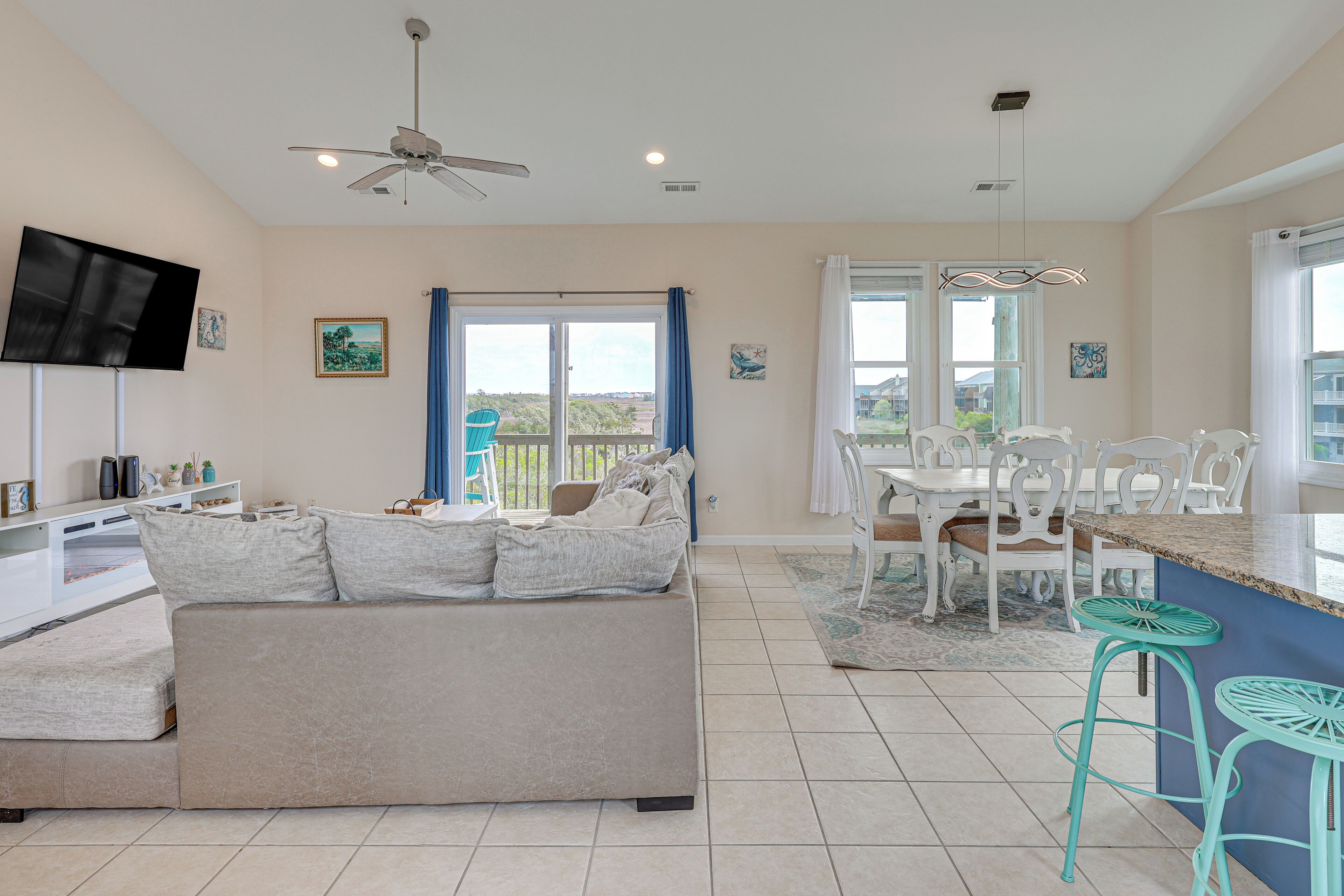 A modern living room with a sofa, TV, ceiling fan, and a dining area with chairs and a table.