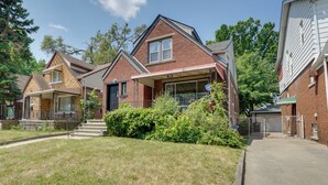 A residential neighborhood with brick houses, a covered porch, and a gated driveway. - Detroit Vacation Rental w/ Porch & Fenced Backyard (Highland Park)