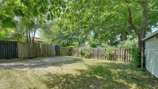 A backyard with a wooden fence, a concrete patio, and a grassy area. - Detroit Vacation Rental w/ Porch & Fenced Backyard (Highland Park)
