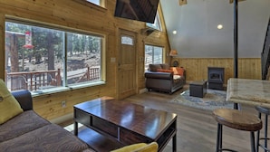 A cozy cabin interior with wooden walls, a large window, a fireplace, and a TV mounted on the ceiling. - Cozy Duck Creek Cabin ~ 12 Mi to Nat'l Forest (Duck Creek Village)