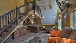 A spacious living area with a wooden staircase, a kitchen with bar stools, and a cozy seating area with a sofa and ottoman. - Cozy Duck Creek Cabin ~ 12 Mi to Nat'l Forest (Duck Creek Village)