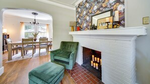Un salon avec une cheminée, un coin repas avec une table et des chaises, et un fauteuil vert.