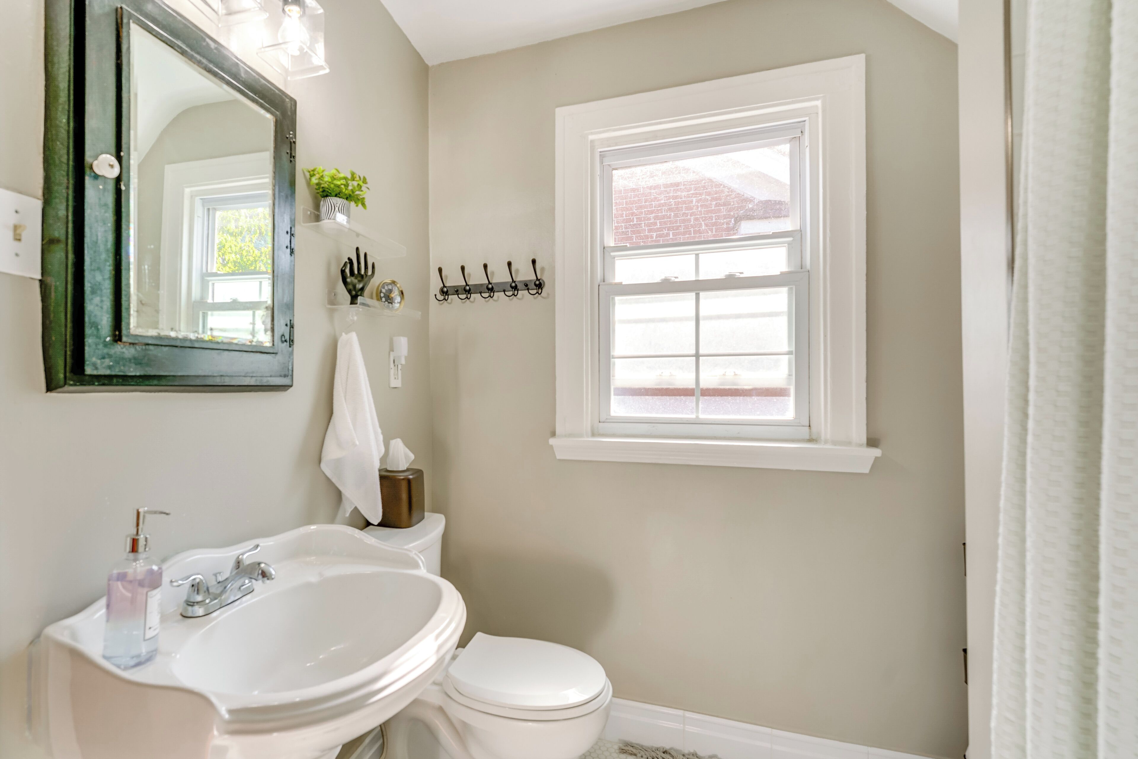 Une salle de bain avec un lavabo blanc, des toilettes, un miroir et une fenêtre.