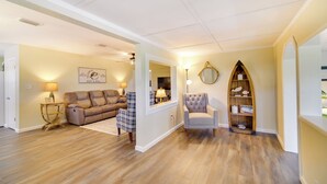 A living room with a brown leather sofa, a plaid armchair, and a white armchair. There is a wooden bookshelf with decorative items and a mirror on the wall. - Lake Wales Vacation Rental w/ Direct Canal Access! (Lake Wales)
