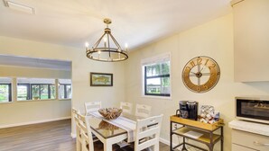 A dining area with a wooden table, white chairs, a chandelier, a clock, and a kitchen area with a microwave and coffee maker. - Lake Wales Vacation Rental w/ Direct Canal Access! (Lake Wales)