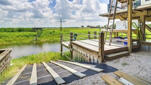 A wooden deck with a metal railing overlooking a river, a ladder, and a small building with a window and a faucet. - Lake Wales Vacation Rental w/ Direct Canal Access! (Lake Wales)