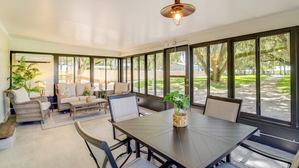 A sunroom with a large table and chairs, surrounded by large windows offering views of a backyard with a wooden deck and greenery. - Lake Wales Vacation Rental w/ Direct Canal Access! (Lake Wales)