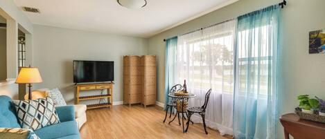 Una sala de estar con sofá, televisor, cesta de mimbre y una mesa con sillas.