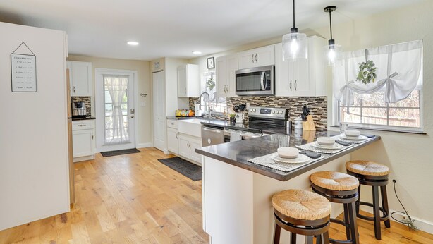 A modern kitchen with white cabinets, a central island with stools, a microwave, and a large window with curtains. - Lake Wales Vacation Rental w/ Screened-in Porch! (Lake Wales)