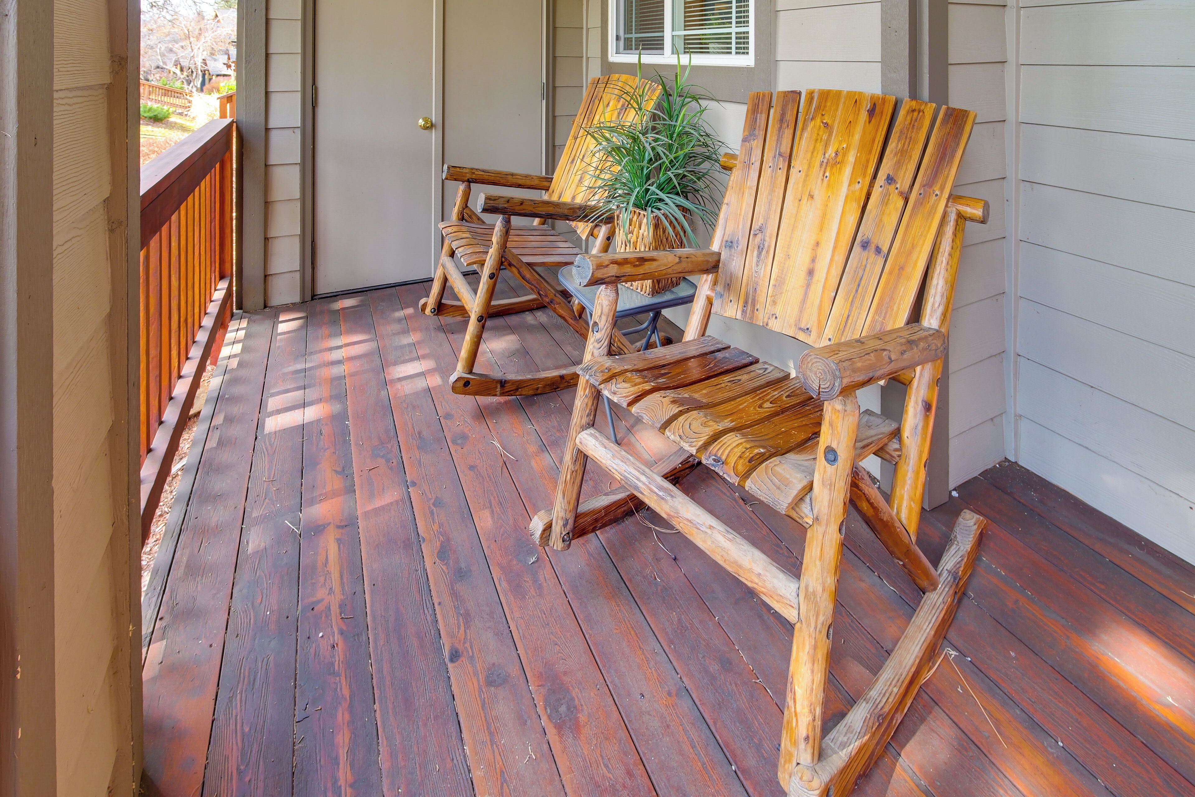 A wooden porch with two rocking chairs and a potted plant.