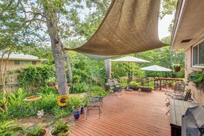 A wooden deck with outdoor furniture, surrounded by lush greenery and a large shade sail. - Lovely Bryan Home w/ Deck - 4 Mi to Kyle Field! (Bryan)