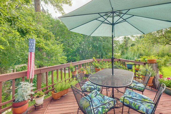 A wooden deck with a table and chairs, surrounded by potted plants and an American flag. - Lovely Bryan Home w/ Deck - 4 Mi to Kyle Field! (Bryan)
