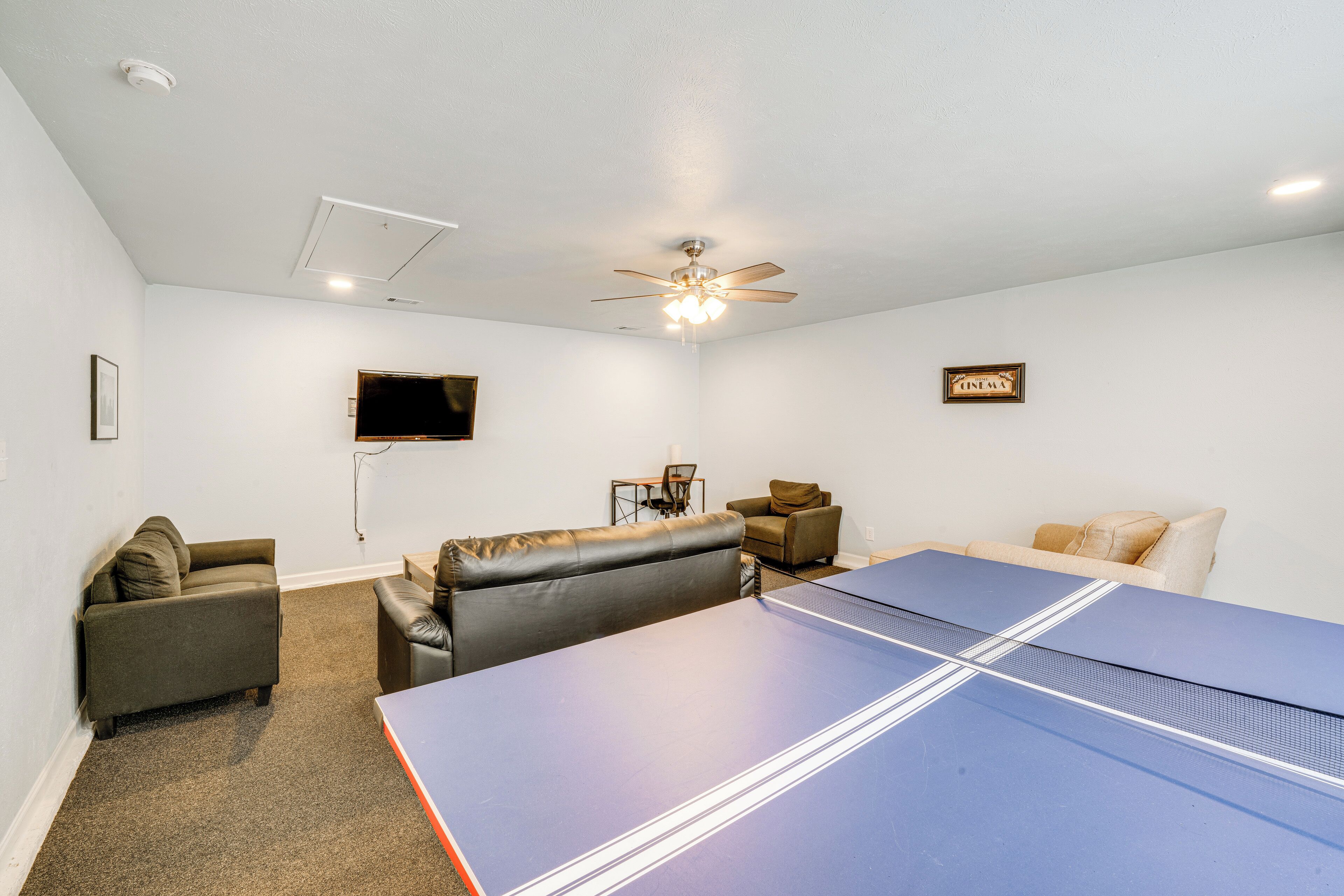 A room with a ping pong table, a ceiling fan, a TV, and a couch.