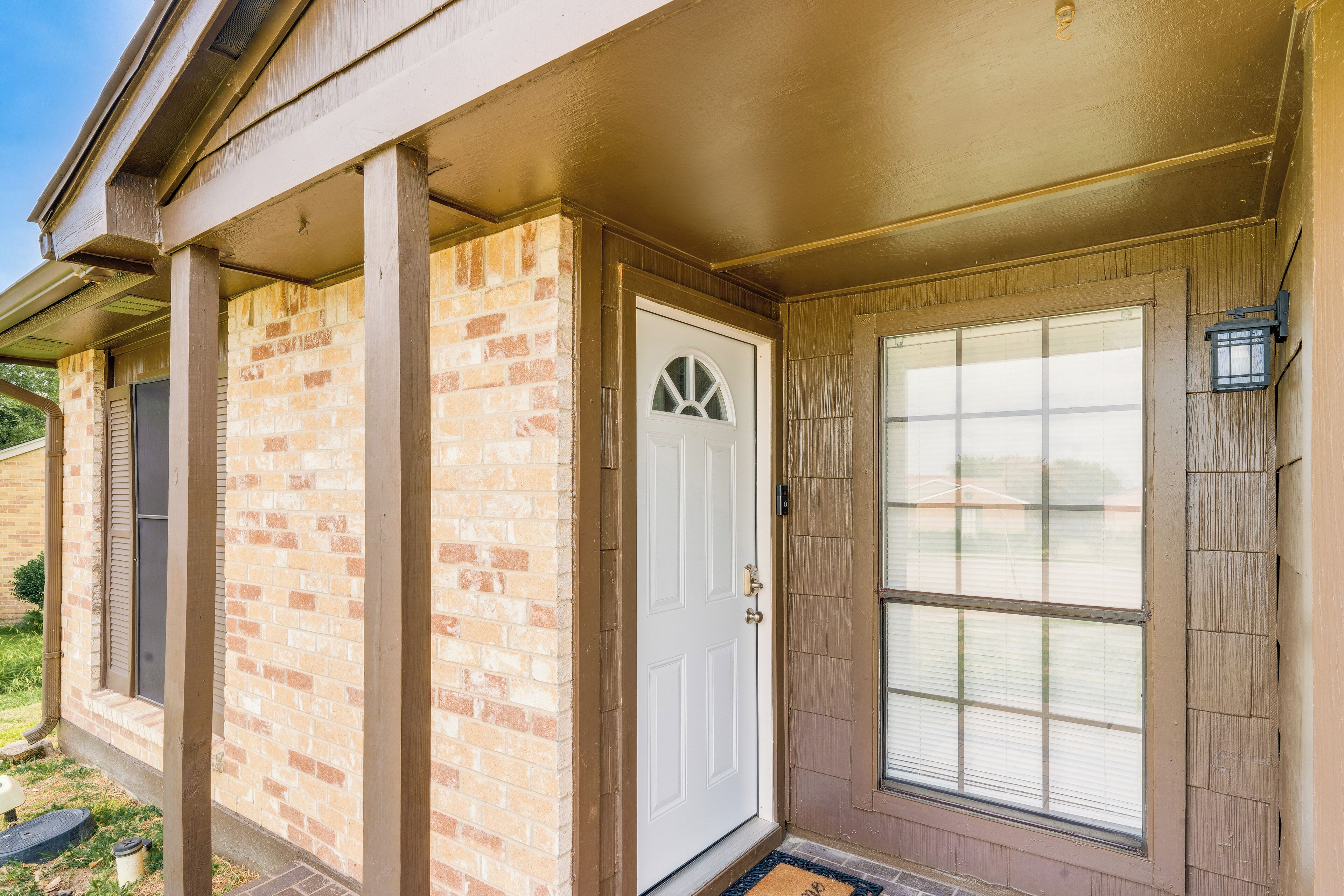 A house with a brick exterior, a white front door, and a large window with blinds.