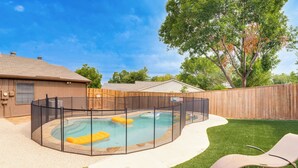 Un jardin avec une piscine, un espace clôturé et une pelouse agrémentée de deux chaises longues.