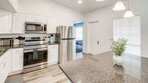 Une cuisine moderne avec des meubles blancs, des appareils en acier inoxydable, des plans de travail en granit et des luminaires suspendus.