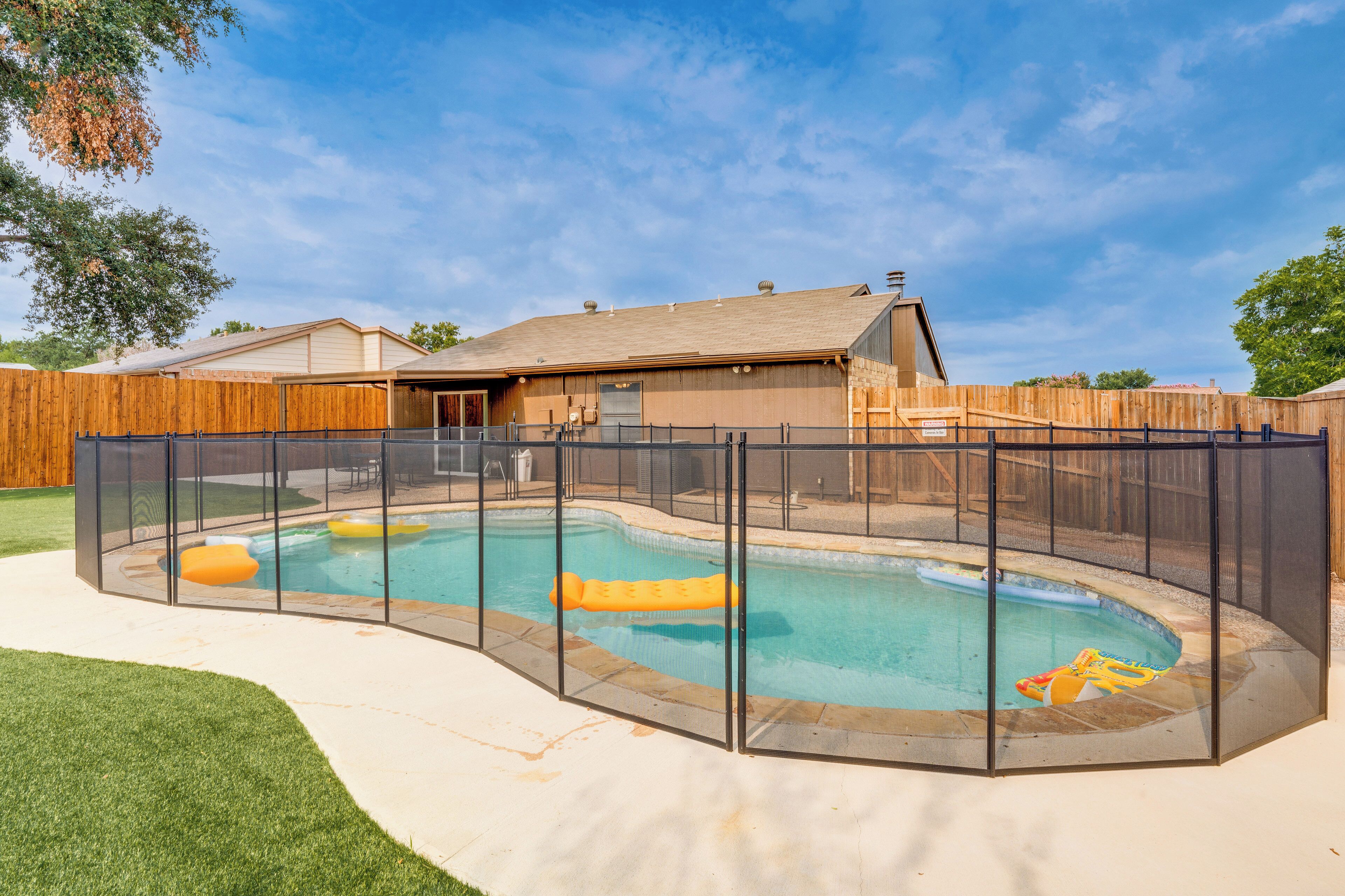 Un patio trasero con piscina, cerca de madera y una casa al fondo.