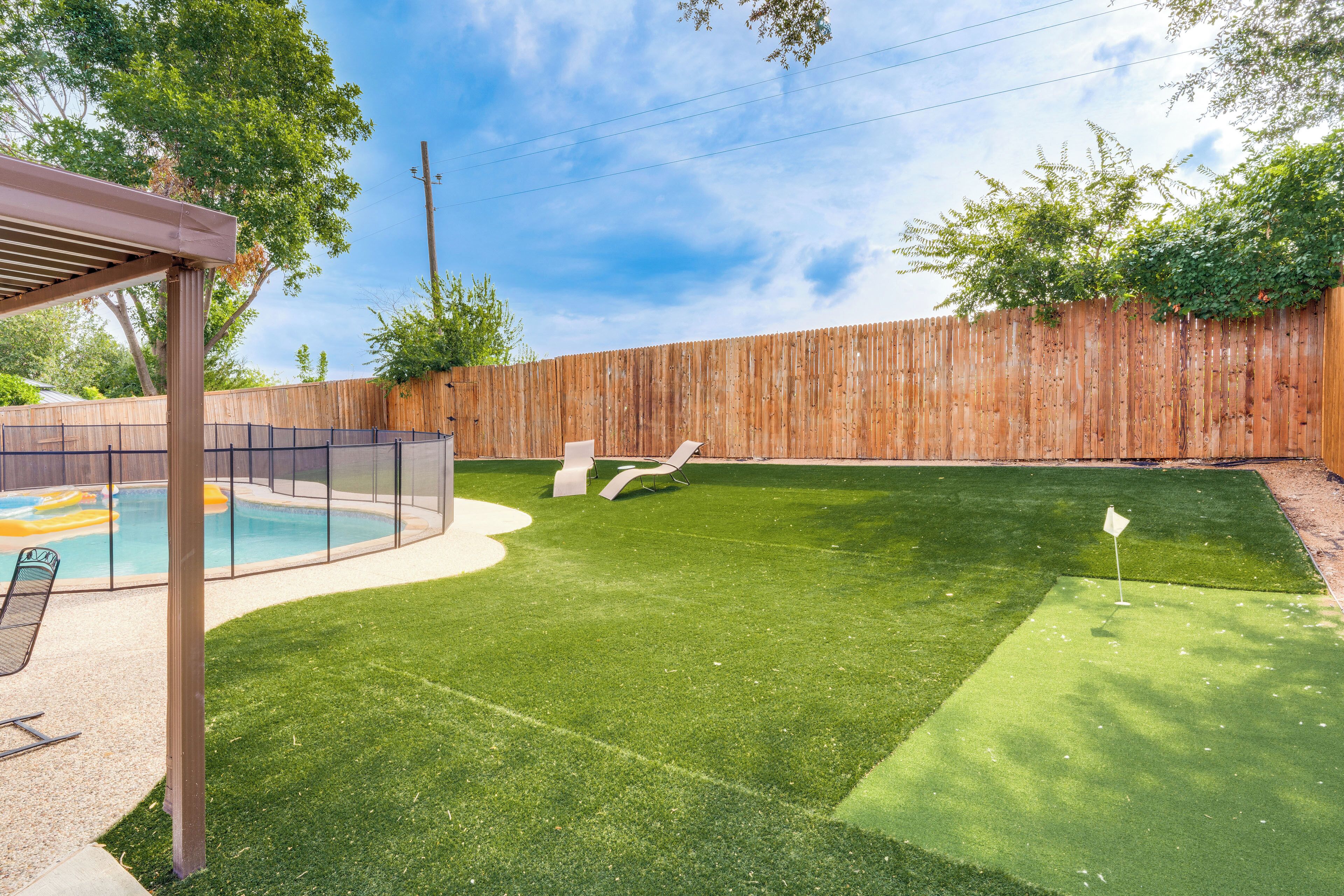 Un patio trasero con piscina, césped artificial y valla de madera.