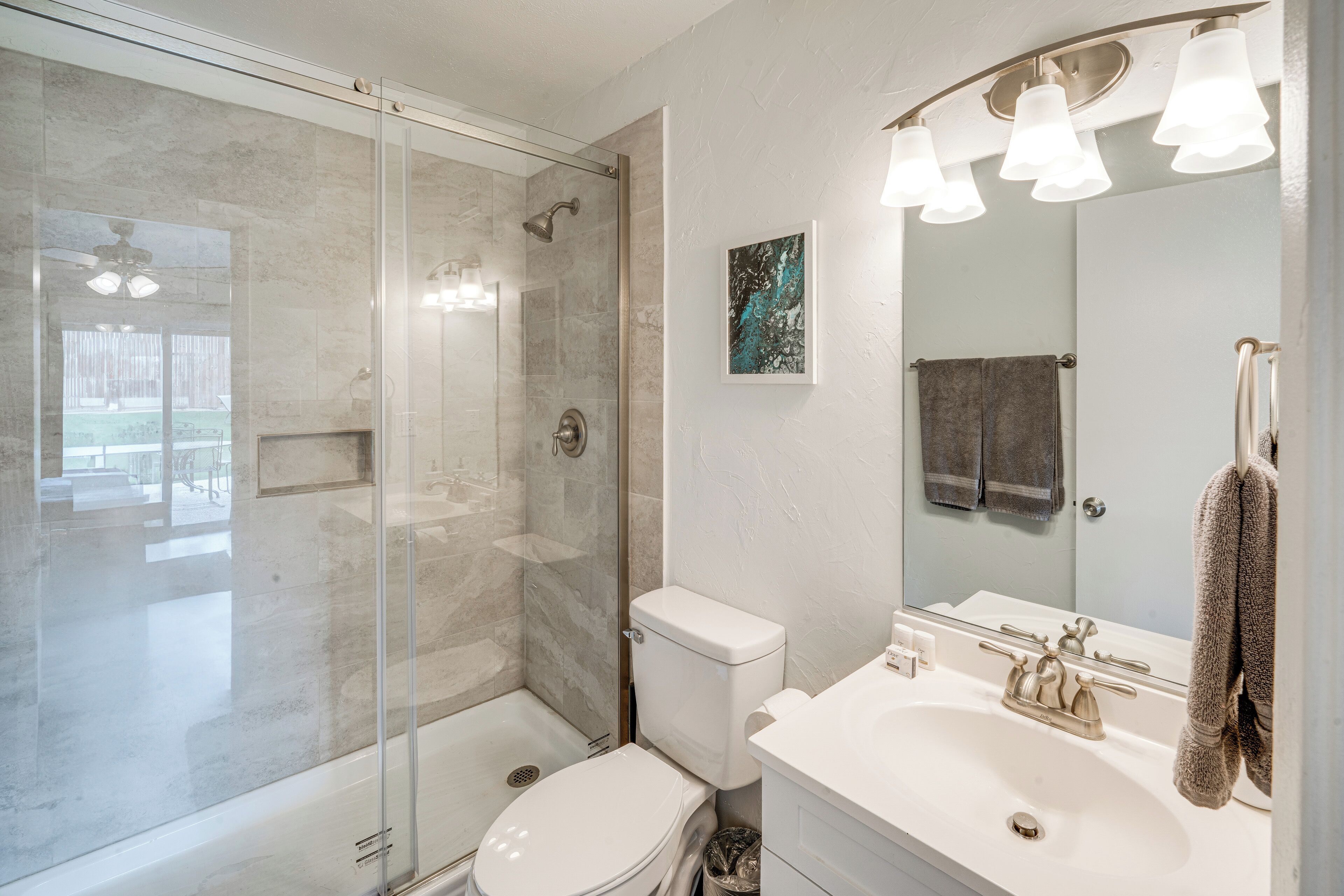 Un baño moderno con ducha envuelta en vidrio, un lavabo blanco y un espejo grande.