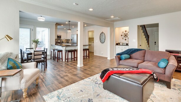 A spacious living room with a brown leather sofa, striped armchair, and ottoman. A dining area with a table and chairs is visible in the background. - < 1 Mi to OU Campus - Norman Vacation Rental (Norman)