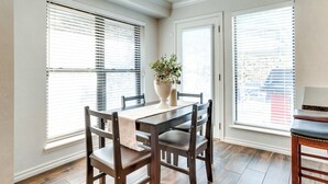 A dining area with a wooden table and chairs, a vase with flowers, and large windows with blinds. - < 1 Mi to OU Campus - Norman Vacation Rental (Norman)