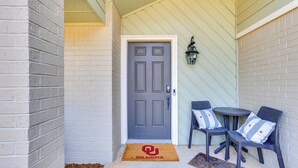 A door with a doormat, a small table, two chairs, and a wall-mounted lamp. - < 1 Mi to OU Campus - Norman Vacation Rental (Norman)