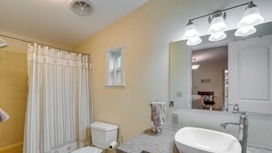 A bathroom with a shower curtain, toilet, sink, and a mirror with lights.