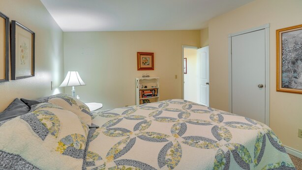 A bedroom with a bed, a nightstand, a lamp, a bookshelf, and a door.