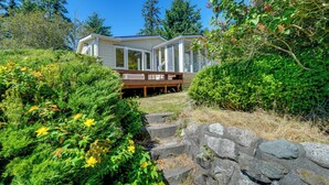 A house with a deck, surrounded by lush greenery and a stone wall.