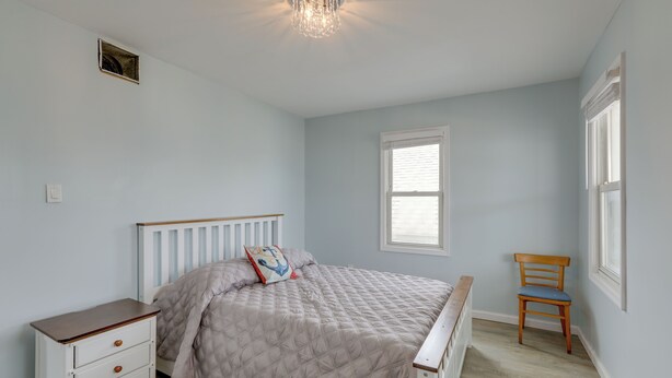 A bedroom with a bed, a nightstand, a chair, and a window. - Sunny Seaside Heights Retreat: Walkable Location! (Seaside Heights)