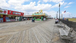 A wooden boardwalk with shops, including a pizza place and a hot dog stand, under a clear sky. - Sunny Seaside Heights Retreat: Walkable Location! (Seaside Heights)